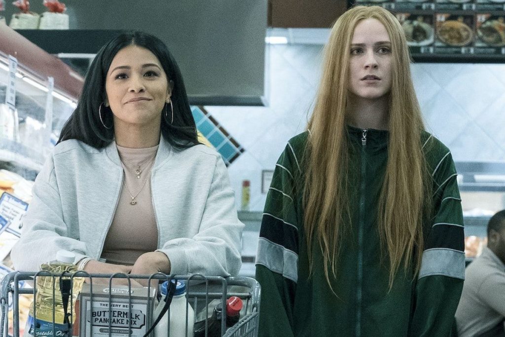 Still from the film Kajillionaire, a woman in a white jacket pushes a shopping cart and another woman walks beside her both facing the camera