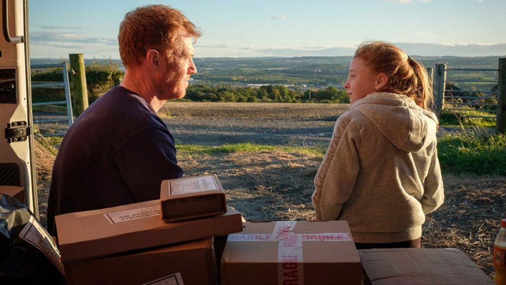 Still from the film Sorry We Missed You, a man sits in the back of a delivery truck with a young girl