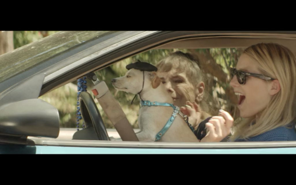 Screen shot from Starlet, medium shot through a car window of a young woman, a dog in beret, and an old woman